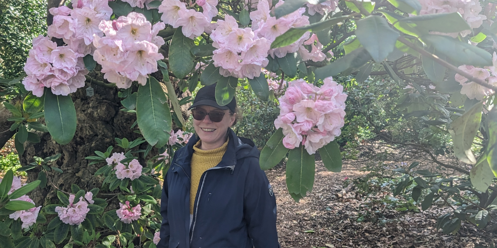 Lisa is standing beneath a large, established rhododendron bush smiling