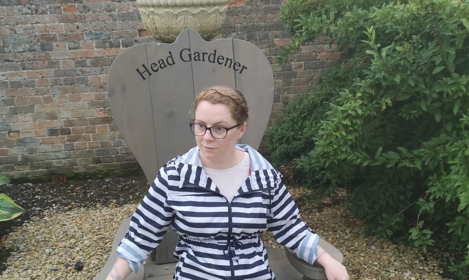 Lisa sitting in a giant chair at Clumber Park, Nottinghamshire, which has the words ‘Head Gardener’ etched into the top.